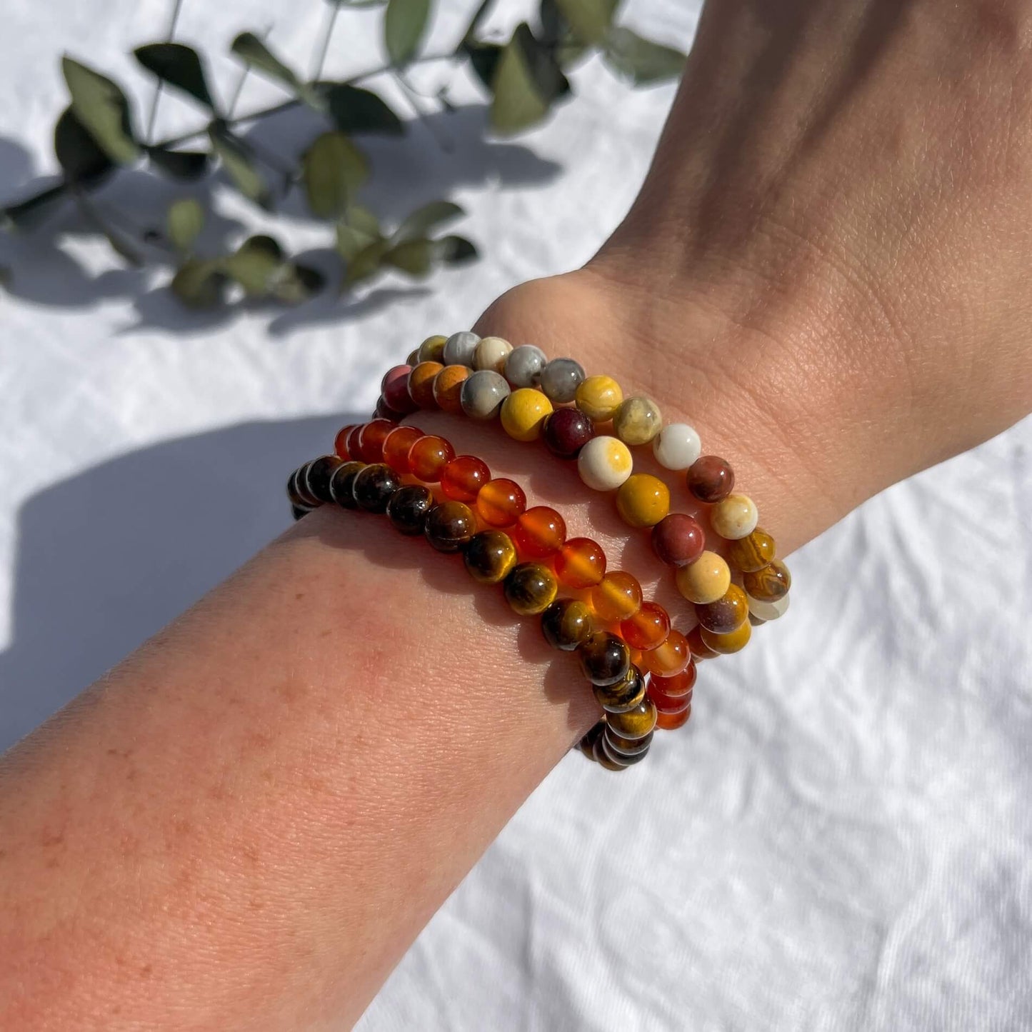 A lady's wrist with vivid white, yellow, orange & red crystal bead bracelets in carnelian, mookaite, tiger's eye and crazy lace agate