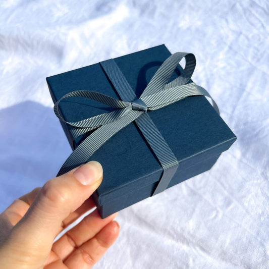 Luxury navy gift box tied in a teal grey ribbon held to camera