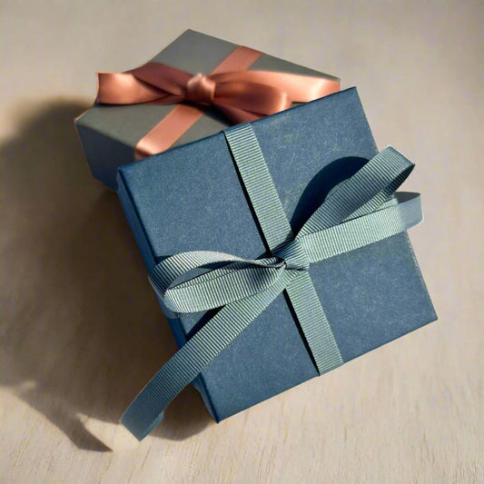 Luxury navy gift box tied in a teal grey ribbon with a grey gift box & pink ribbon in the background