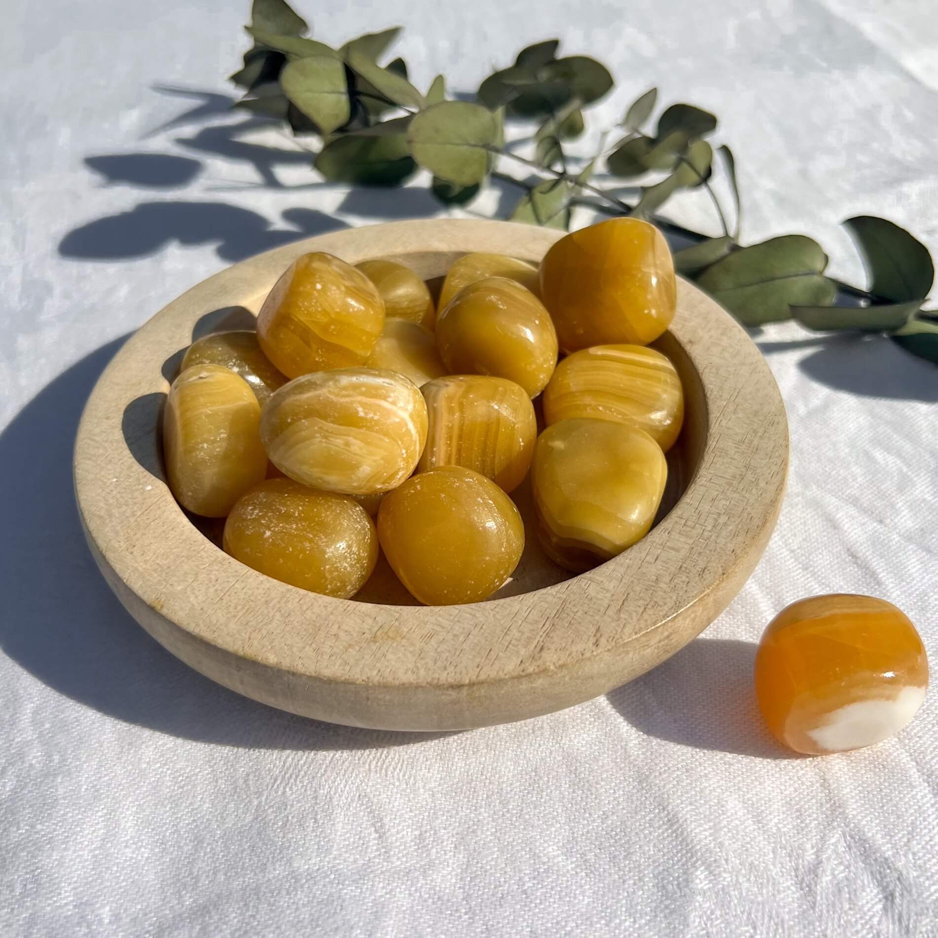 A wooden dish filled with bright glossy orange calcite crystal pebbles gleaming in the sun