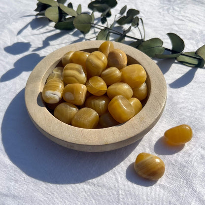 Striped orange and honey coloured Orange Calcite crystal tumble stones gleam in the sun in a wooden dish