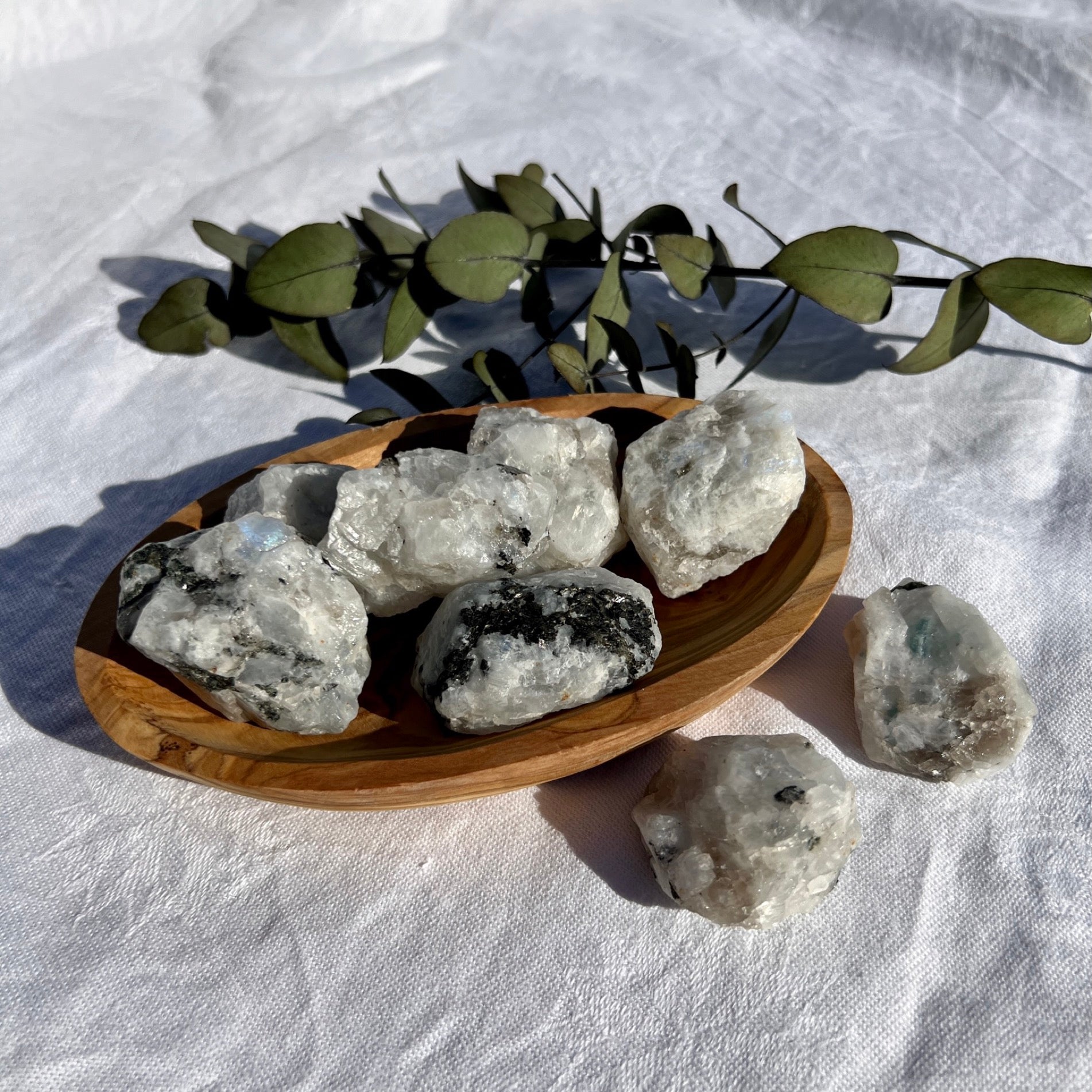Wooden bowl filled with small raw chunks of flashy rainbow moonstone crystals
