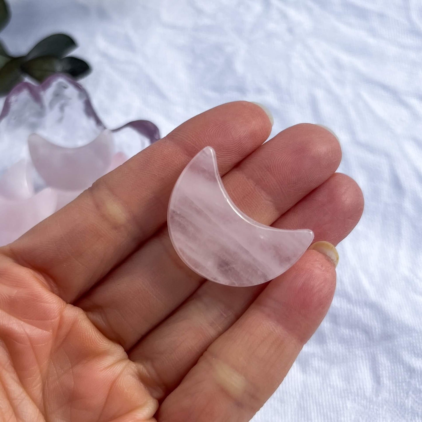 A pale pink carved crystal rose quartz mini moon in an open hand