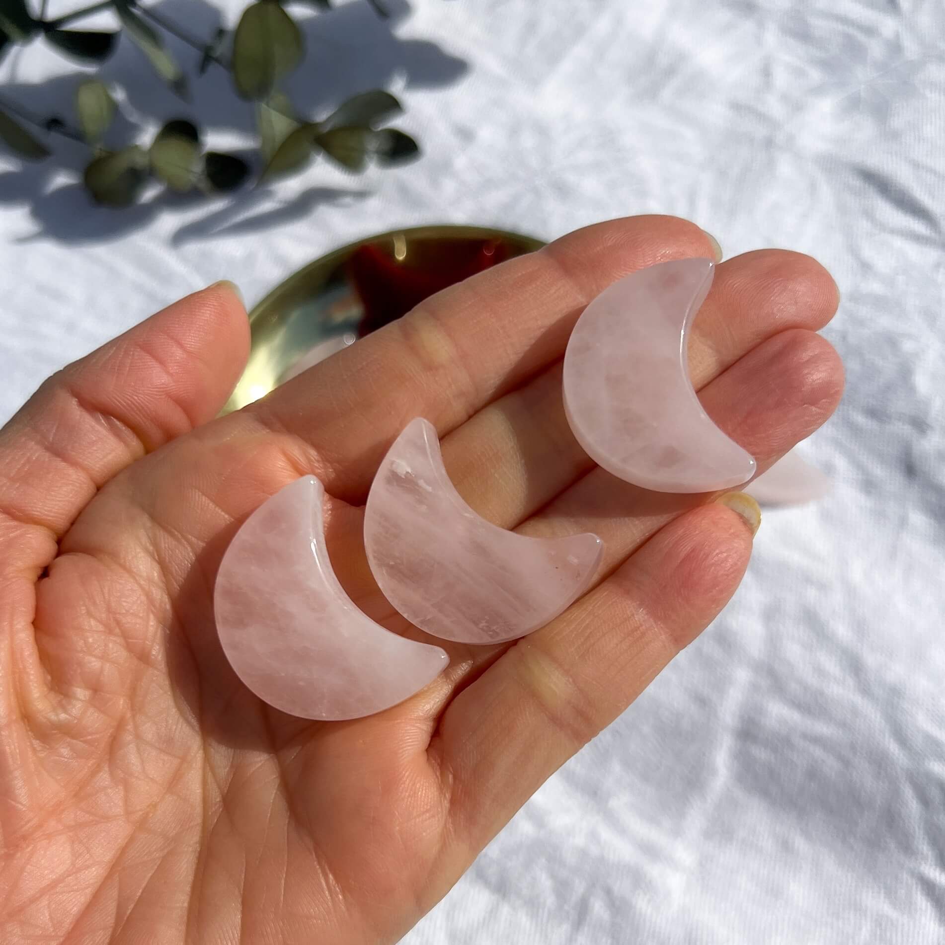 Three pale pink carved crystal rose quartz mini moons displayed on an open hand