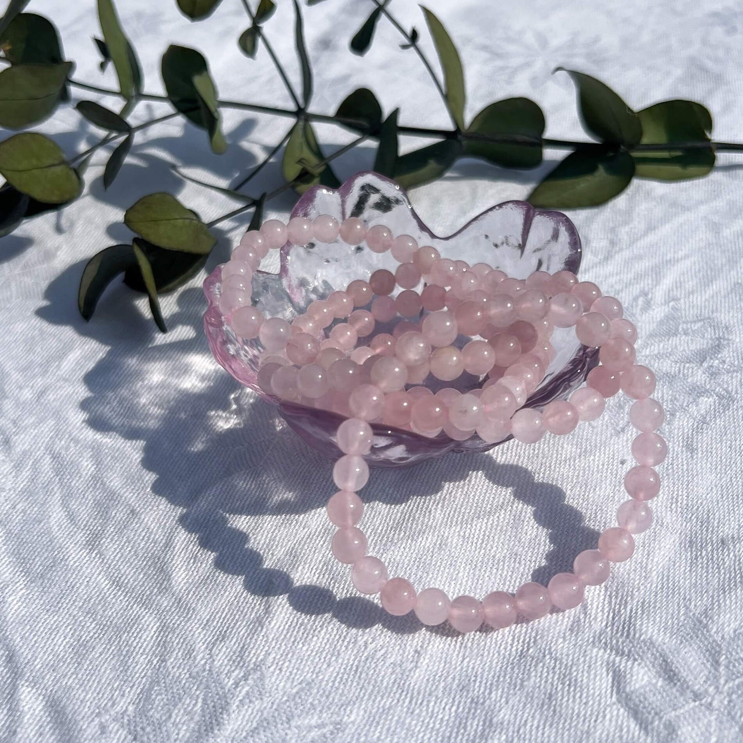 A glass trinket dish filled with pink coloured rose quartz crystal bead bracelets