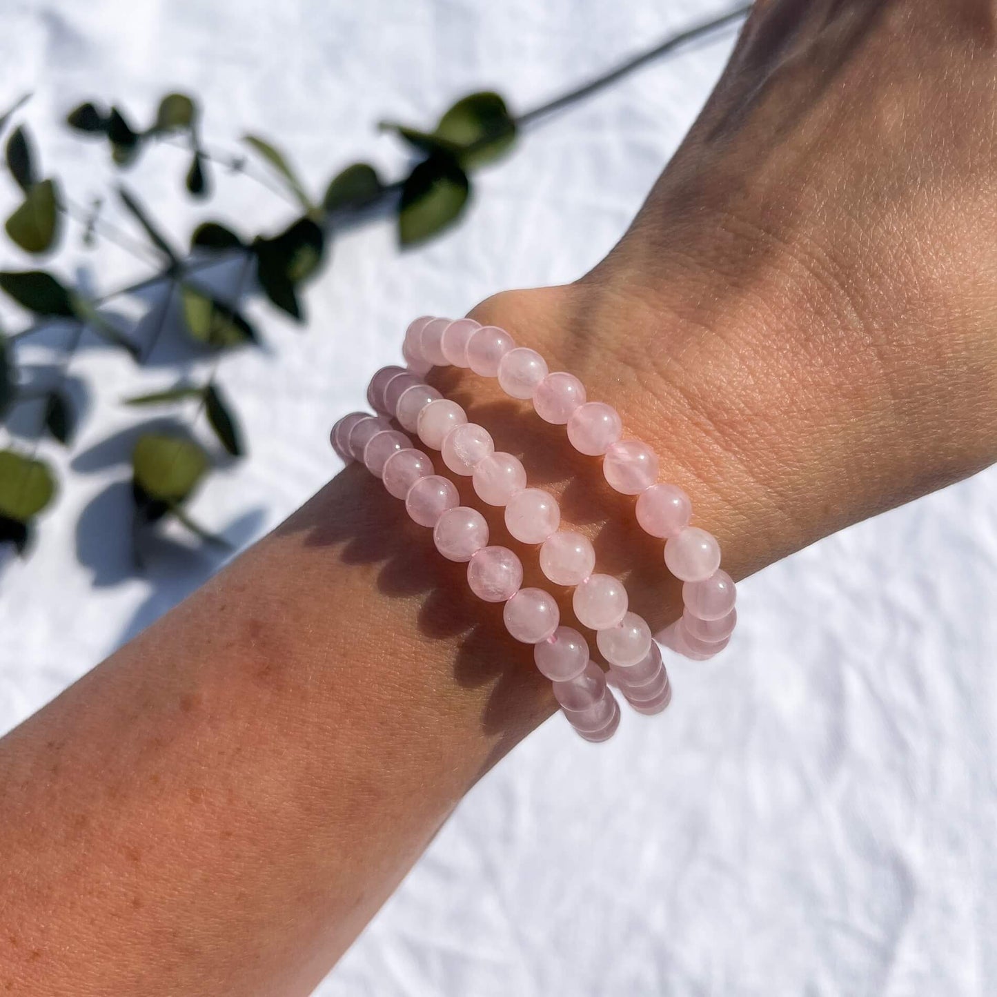 A woman's arm wearing 3 pink coloured rose quartz crystal bead bracelets