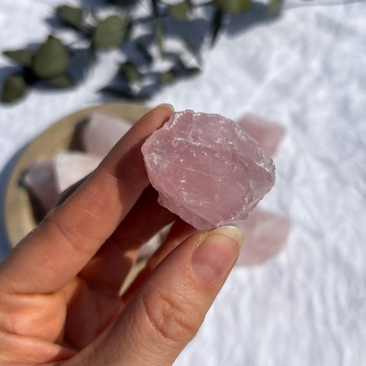 A bright pink raw rose quartz crystal piece held to camera