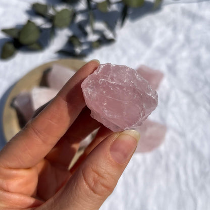 A bright pink raw rose quartz crystal piece held to camera