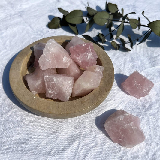 A wooden dish overflowing with bright pink raw rose quartz crystal pieces
