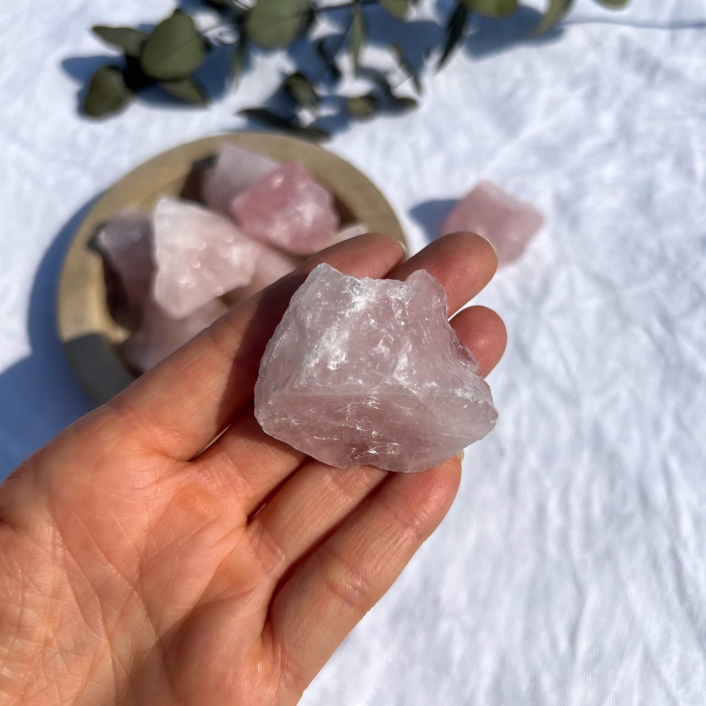 A hand holding a bright pink raw rose quartz crystal piece