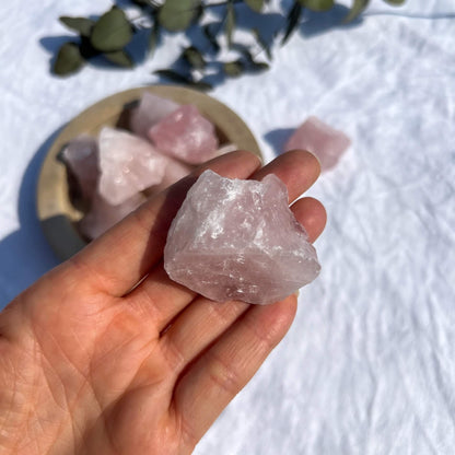 A hand holding a bright pink raw rose quartz crystal piece