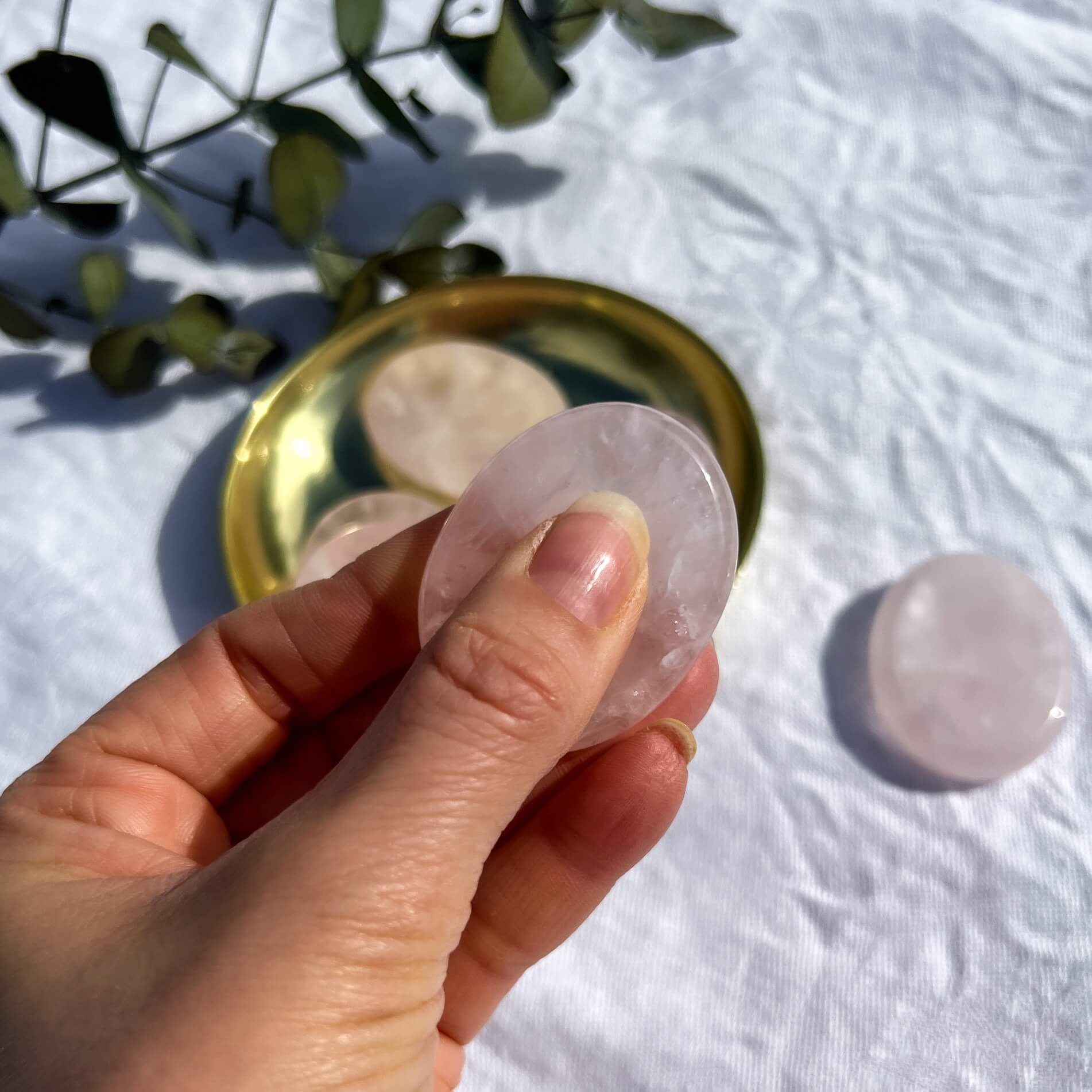 Pale pink gemmy rose quartz crystal oval worry stone pinched between thumb and fingers