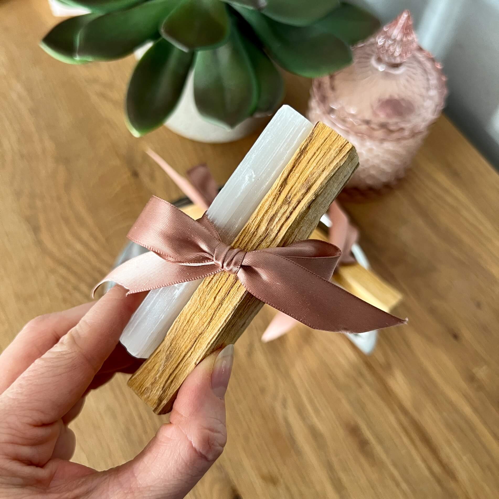 Palo Santo and Selenite sticks tied with pretty pink ribbon held to camera