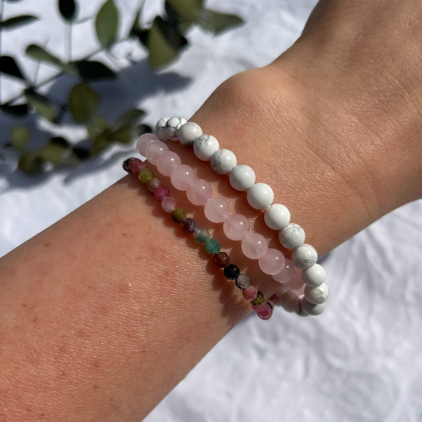 A woman's arm wearing three self love crystal bead bracelets in howlite, mixed tourmaline and rose quartz