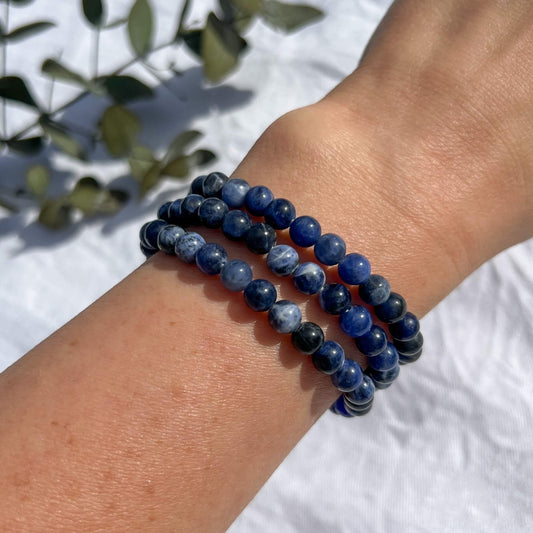 Three blue and white patterned Sodalite crystal bead bracelets worn on a wrist held close to the camera