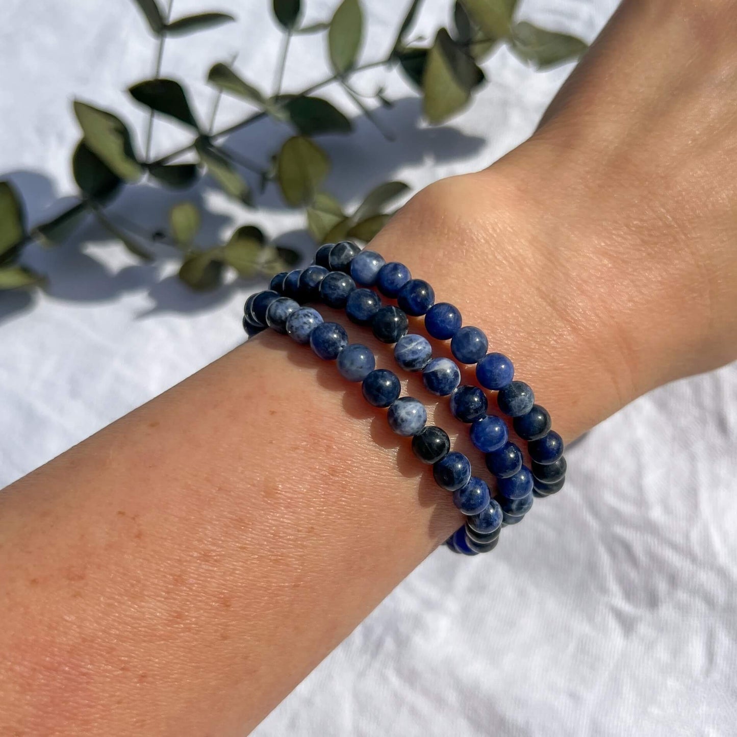 A woman's wrist wearing Three blue and white patterned Sodalite crystal bead bracelets