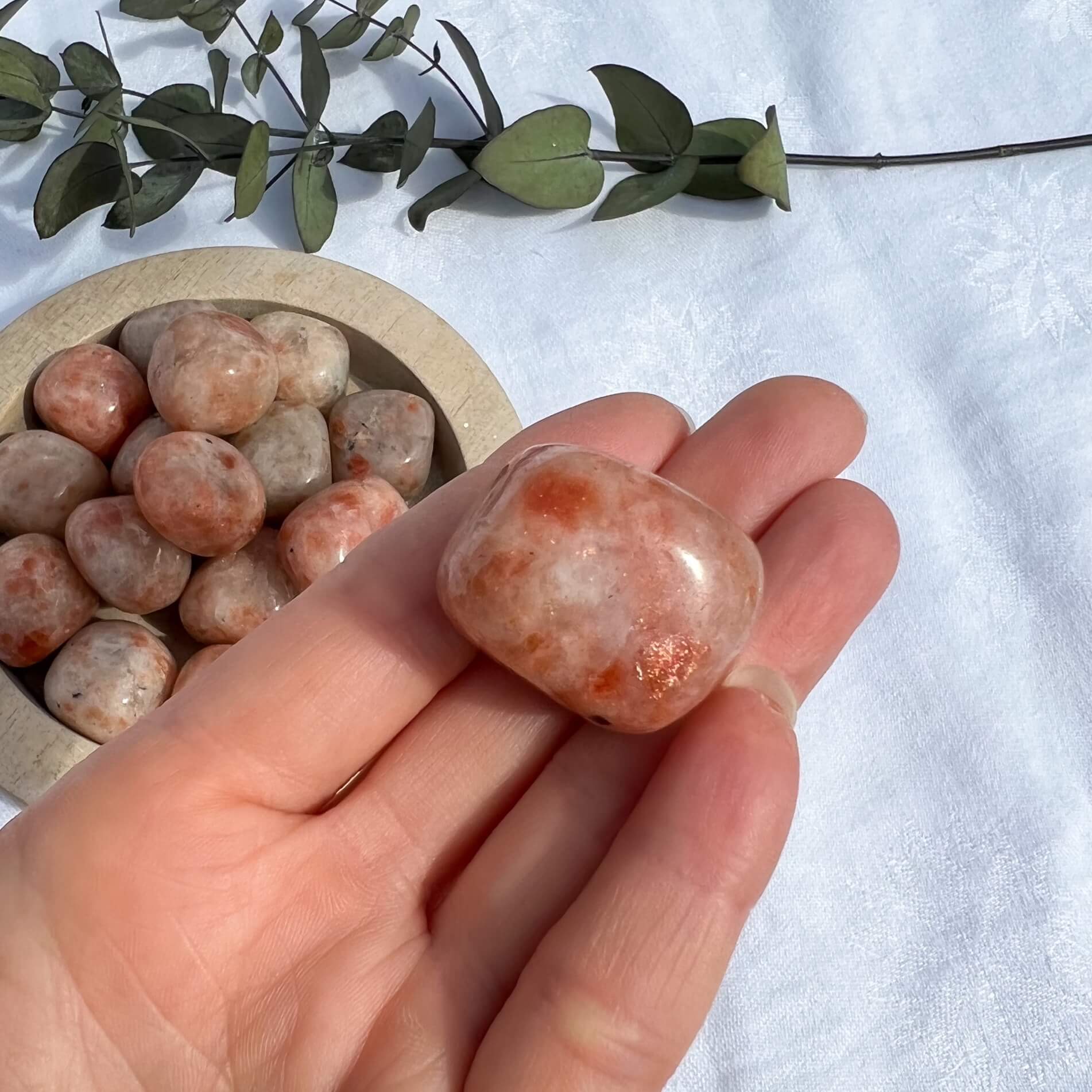 Bright orange sparkly sunstone crystal pebble held in an outstretched hand