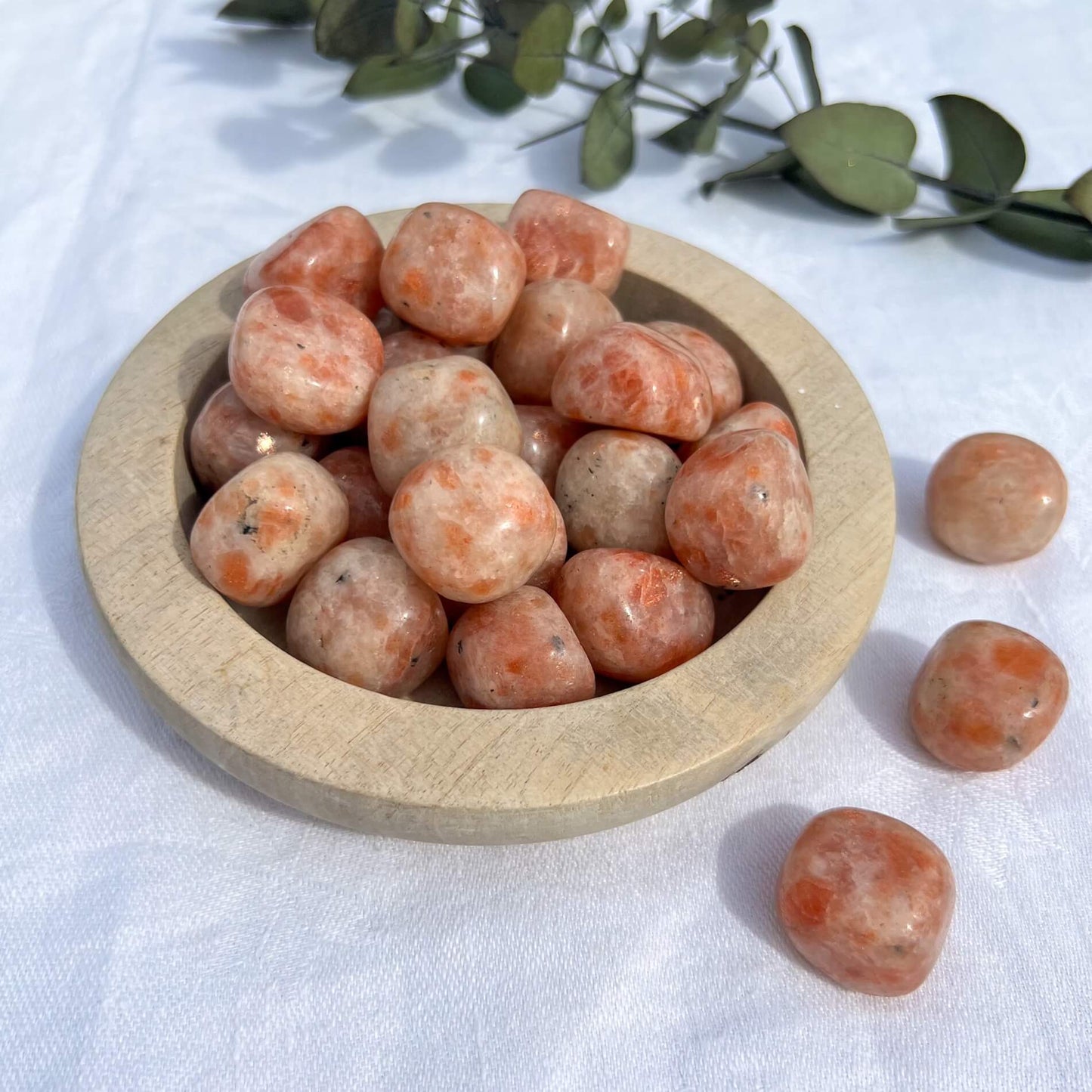 Bright and cheerful orange coloured sunstone crystal tumble stones spilling from a wooden dish