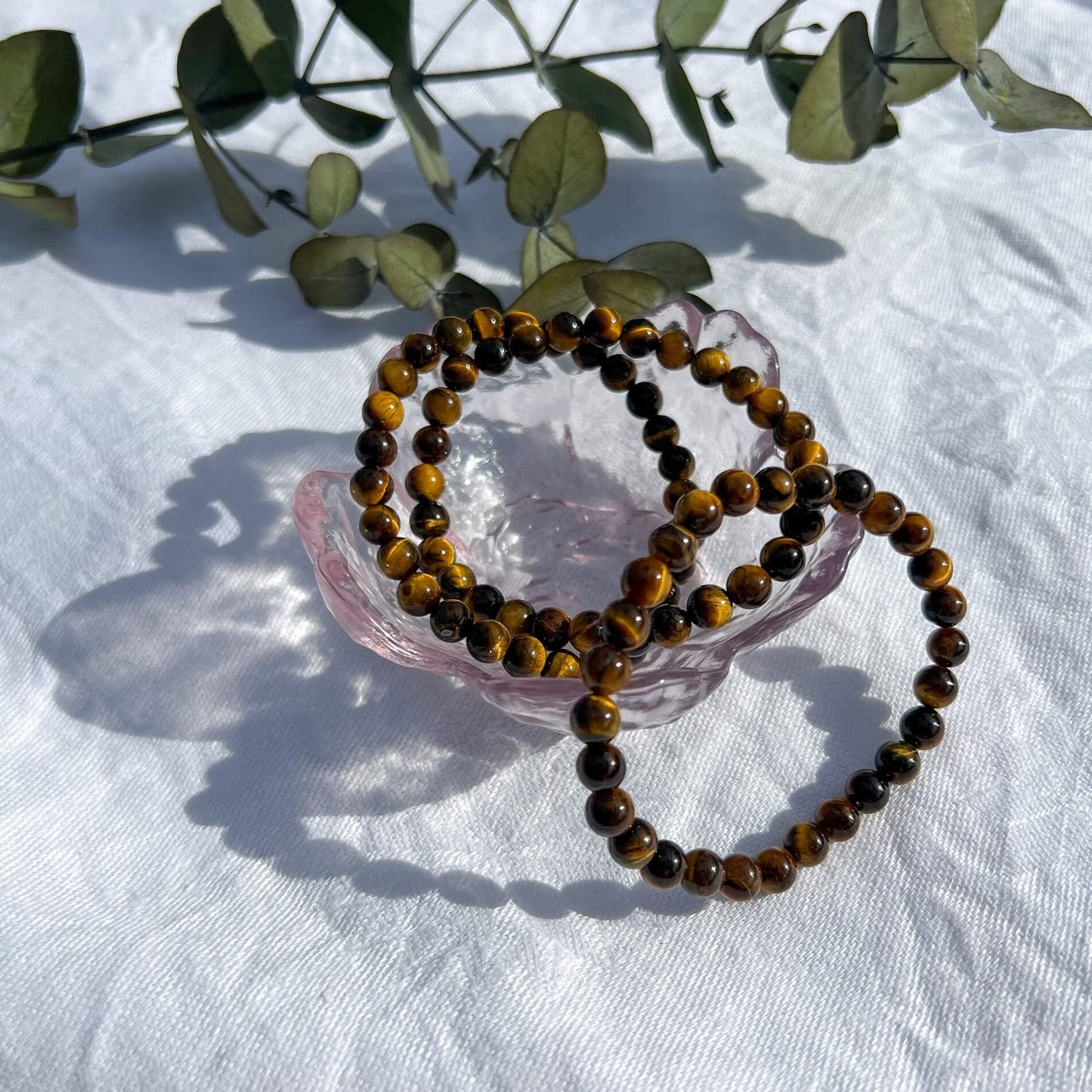 A glass dish filled with brown and golden tiger's eye healing crystal bead bracelets