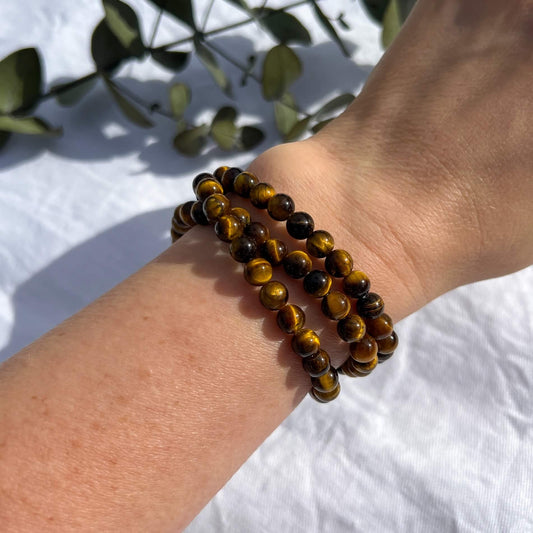 A woman's wrist wearing brown and golden tiger's eye healing crystal bead bracelets